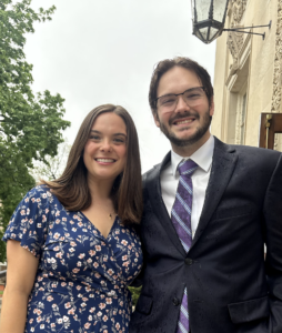 Picture of Grace and Blake standing outside Kirby Hall in a dress and suit on a wet day.